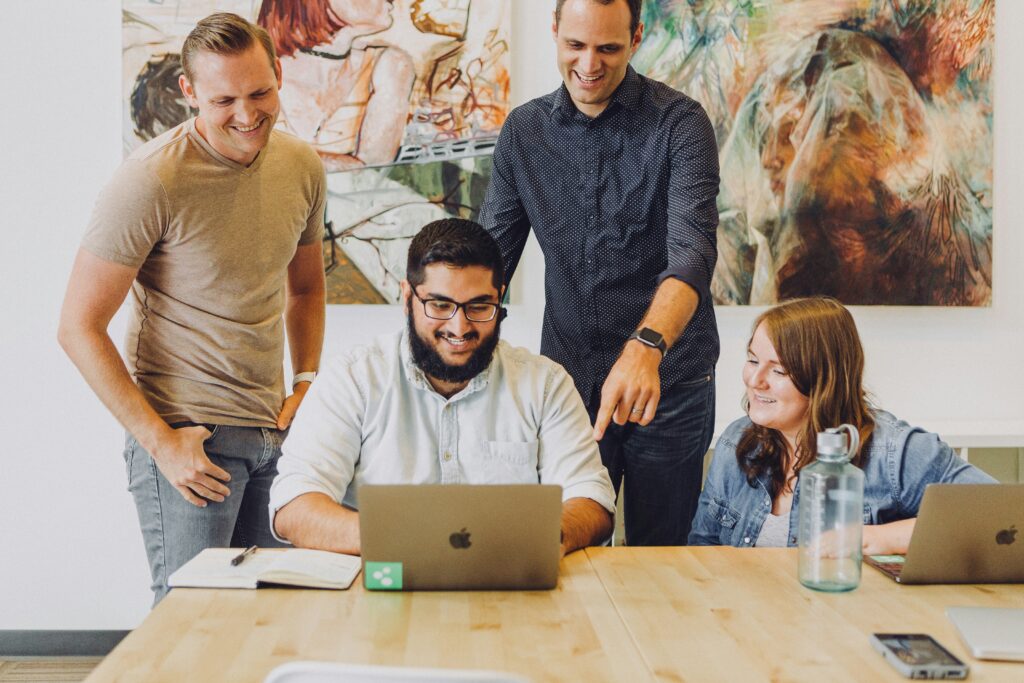 four coworkers smiling around laptop at table